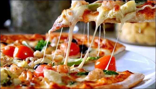 A slice lifted from a pizza with melted cheese and colourful toppings